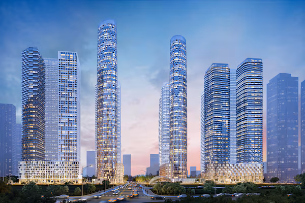 An architectural rendering depicting futuristic high-rise residential towers and office buildings illuminated at dusk. The towers line a wide street with streetlights and light traffic, showcasing a dense urban skyline against a soft purple and blue sky.